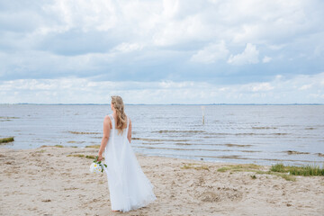 Fototapeta na wymiar bride on the beach. Bride in dress looks to the sea. Getting married at the North Sea. Beach wedding in Germany 