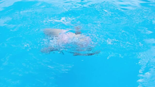 Girl somersaults and plays in the transparent blue swimming pool water. Child have fun in swim pool. Full HD slow motion video.