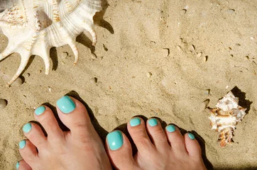 Poster Summer beach concept with female legs and shells on sand. Turquoise nail polish. Nice pedicure fingers. Health and body care. Place for your text. © dore art