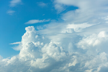 Towering form of cumulonimbus rain cloud contrasted against a vibrant blue sky rising up and lit up from below. Weather conditions and climate detail background.