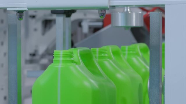 Empty green plastic jerrycans falling from conveyor belt of pet blow molding machine at factory, exhibition - close up. Manufacturing, recycling, industry, automated technology equipment concept