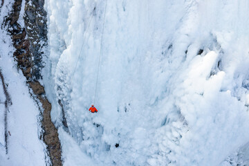 Aerial shot of an ice slope bumps, ridges, and icicles by which climbing up man using traction ice tool technique
