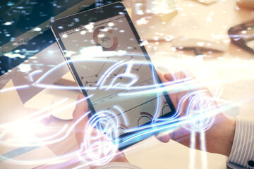 Double exposure of man's hands holding and using a digital device and automobile theme hologram drawing. Technology concept.