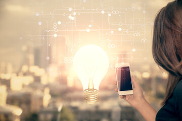 Double exposure of light bulb hologram and woman holding and using a mobile device. Idea concept.