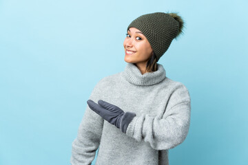 Young Uruguayan girl with winter hat isolated on blue background extending hands to the side for inviting to come