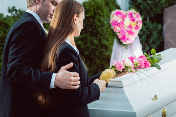 Mourning man and woman on funeral with pink rose standing at casket or coffin