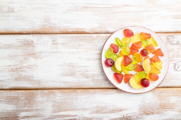 Various fruit candies on plate on white wooden background. copy space, top view.