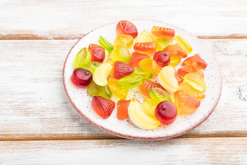 Various fruit candies on plate on white wooden background. close up, side view.