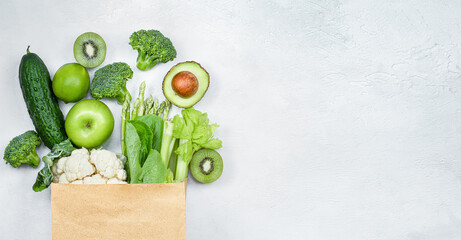 green vegetables and fruits in a paper bag on a light gray background