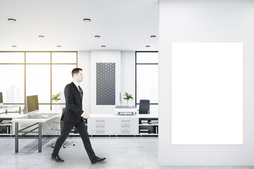 Fototapeta premium Businessman walking in bright coworking office interior with empty banner, window and city view, daylight, furniture and equipment. Mock up.