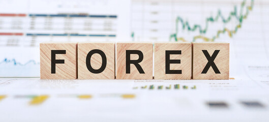 Word FOREX made with wood building blocks on background from financial graphs and charts.