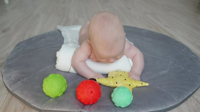 Cute baby lying on his tummy on play mat, 3 month old newborn infant boy playing with colorful sensory balls on the floor. High quality 4k footage