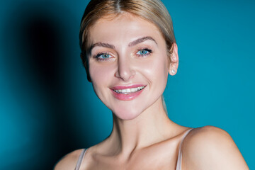 Perfect shiny smile. A happy laughing young woman with perfect skin, natural make-up and a beautiful smile. Female portrait with bare shoulders on a blue background.