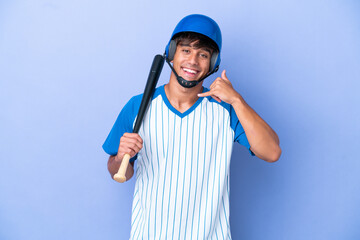 Baseball caucasian man player with helmet and bat isolated on blue background making phone gesture. Call me back sign