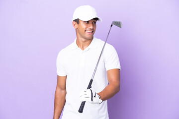 Young caucasian man isolated on purple background playing golf