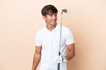Young golfer player man isolated on ocher background looking to the side and smiling