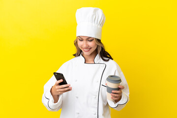 Young Russian chef girl isolated on yellow background holding coffee to take away and a mobile