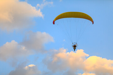 yellow paraglider with a motor at sunset on a background of clouds view from the back
