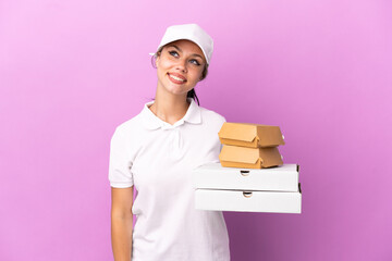 Pizza delivery Russian girl with work uniform picking up pizza boxes and burgers isolated on purple background thinking an idea while looking up