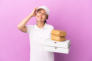 Pizza delivery Russian girl with work uniform picking up pizza boxes and burgers isolated on purple...