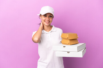 Pizza delivery Russian girl with work uniform picking up pizza boxes and burgers isolated on purple background laughing