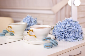 Cup of tea, macaroons and blue hydrangea flower on beauty salon background
