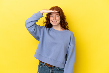 Teenager reddish woman isolated on yellow background looking far away with hand to look something