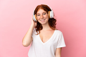 Teenager reddish woman isolated on pink background listening music