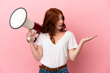 Teenager reddish woman isolated on pink background holding a megaphone and with surprise facial expression