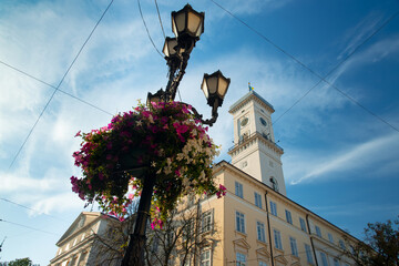 Fototapeta na wymiar city landscaping town hall building and tower with street lantern and hanging flowers perspective foreshortening photography from below with blue sky background in sun rise morning time