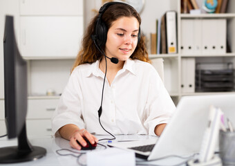 Smiling young brown-haired woman at her workplace using video chat to communicate on a project