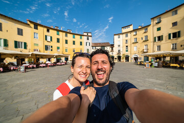 Travel tourists friends taking photo selfi with smartphone in Lucca, Tuscany. happy couple in love traveling in Europe having fun taking self-portrait picture traveling in Italy - obrazy, fototapety, plakaty