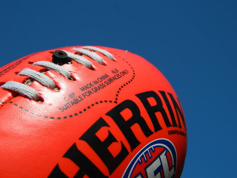Close up of an Australian rules red Sherrin Football on a blue sky background