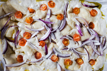 vegan homemade focaccia bread with cherry tomatoes and onions before being cooked, healthy plant-based food