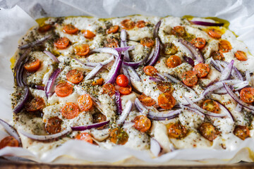 vegan homemade focaccia bread with cherry tomatoes and onions before being cooked, healthy...