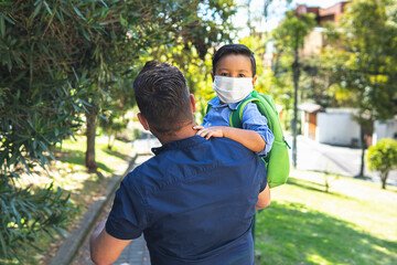 Father carries his son with a mask in his arms to take him to school