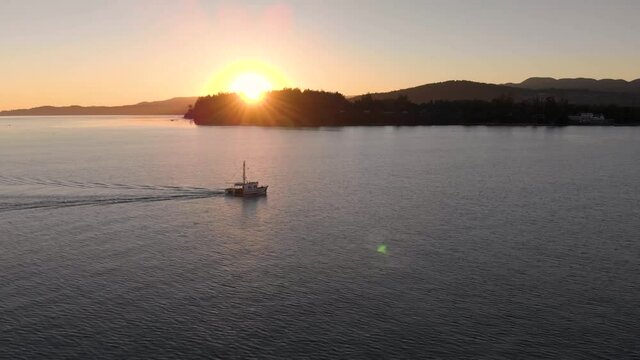 A aerial drone shot of a lone fishing trawler with sunset and coastline in the distance near Sooke, BC. 4K 24FPS.