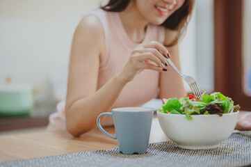 Cropped shot of happy woman eating fresh vegetable salad in white bowl in kitchen.  enjoying a healthy food