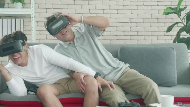 Happy family with son and father play vr headsets video game with excited and fun together on sofa at home, elderly and young man activity using simulation virtual reality with entertainment.