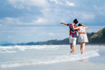 Happy Asian people on beach travel vacation. Young couple holding hand and walking together on the beach in summer sunny day. Boyfriend and girlfriend enjoy and having fun outdoor lifestyle activity.