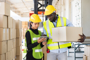 African American and Asian workers wearing safety vest while working in warehouse checking for the inventory