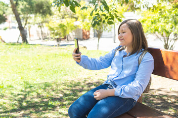 Obraz premium Blonde girl taking a selfie with her cell phone sitting on a park bench