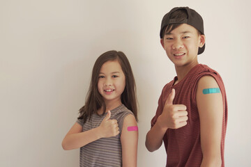 Mixed Asian young girl and teen boy giving thumb up and showing their arms with blue bandage after got vaccinated or  inoculation, child immunization, covid delta vaccine concept - obrazy, fototapety, plakaty