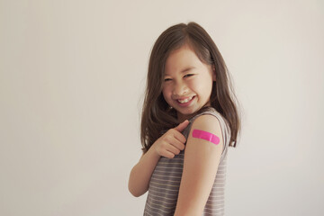 Mixed Asian young girl showing her arm with pink bandage after got vaccinated or  inoculation,...