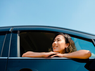Happy Asian woman with short hair traveling by car. Attractive female travelers enjoy and smiling while looking at the view outside with sunshine, summertime.