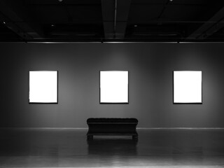 Three mockup white blank museum art frames on dark grey wall background with lighting and empty...