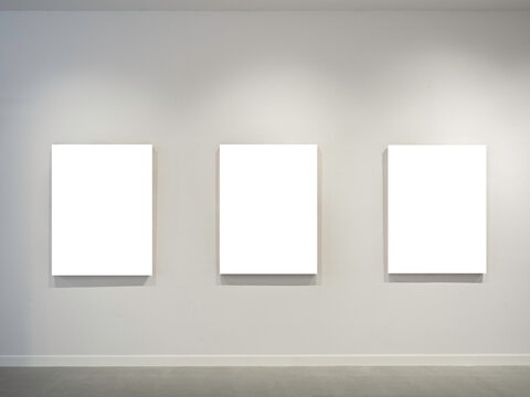 Three mockup white blank museum art frames on white clean wall background with lighting.