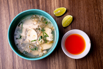 Close-up photo of Soto Seger, one of the Indonesian specialties, made from chicken in a soup-like sauce, accompanied by chili sauce, lime juice, and a wooden textured background