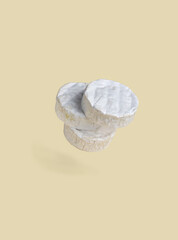 Three wheels of Camembert cheese with white noble mold on pastel yellow background. Food levitation.
