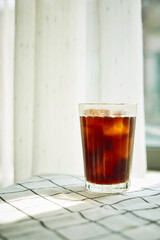 Cold brew cofee with ice on checked cloth beside a window with white curtain